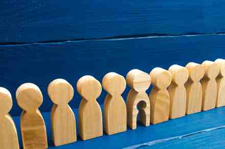 Holzfiguren in einer Reihe, eine hat ein ausgeschnittenes Kind